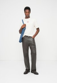 Ανοιχτό μπεζ μπλουζάκι με κόκκινο κείμενο, σε συνδυασμό με σκούρο γκρι, κομψό δερμάτινο παντελόνι. Μια μπλε τζιν τσάντα είναι περασμένη στον ώμο.