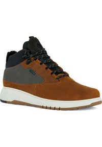 Zapatilla deportiva de caña alta en cuero marrón y malla gris con acentos negros, cierre de cordones, suela acolchada y detalles texturizados en la parte superior.