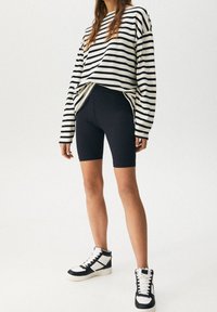 Pasiasta czarno-biała, oversize'owa koszula z długim rękawem, czarne szorty rowerowe i czarne sneakersy za kostkę z białymi akcentami. Gładkie materiały.