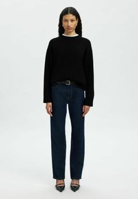 Svart oversized tröja, mörkblå raka jeans och spetsiga svarta klackar. Slät tyg, avslappnad passform och en minimalistisk design.