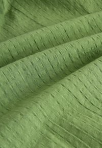 Teksturoitu vihreä kangas, jossa on pehmeä, kudottu pinta, jossa on hienovaraisia uria ja tasainen väri kauttaaltaan. Sopii erilaisiin tekstiilisovelluksiin.