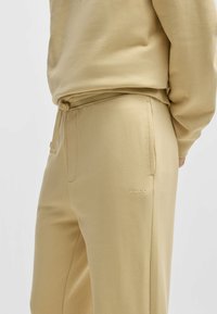 Tan joggers van zacht materiaal, met een trekkoord in de taille, zijzakken en een subtiel reliëf 'HUGO' logo op de dij.