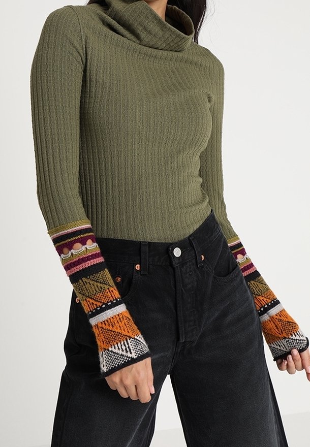 Olivgrön ribbad polotröja med merfärgade geometriska mönstrade vid ärmar, parat med högmidjade svarta jeans.