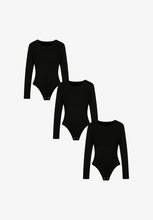 Frau mit glattem dunklem Haar, die einen eng anliegenden schwarzen Langarm-Body trägt und mit einer Hand an der Stirn steht.