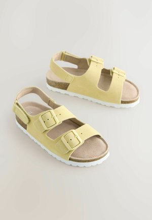 Yellow suede sandals with two adjustable buckle straps, a cushioned footbed, and a white rubber sole. Open heel design for breathability.