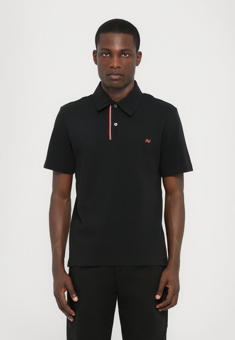 Polo noir en coton avec des manches courtes, doté d'une patte de boutonnage à deux boutons et d'une rayure rouge contrastante le long du col.