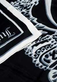 Foulard nero con motivi ornate di bianco e grigio. I bordi presentano un contorno bianco. Il materiale sembra morbido e leggero.