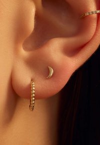 Boucle d'oreille en forme de croissant de lune doré associée à une petite boucle d'oreille texturée sur une oreille, mettant en valeur une finition lisse et un design délicat.