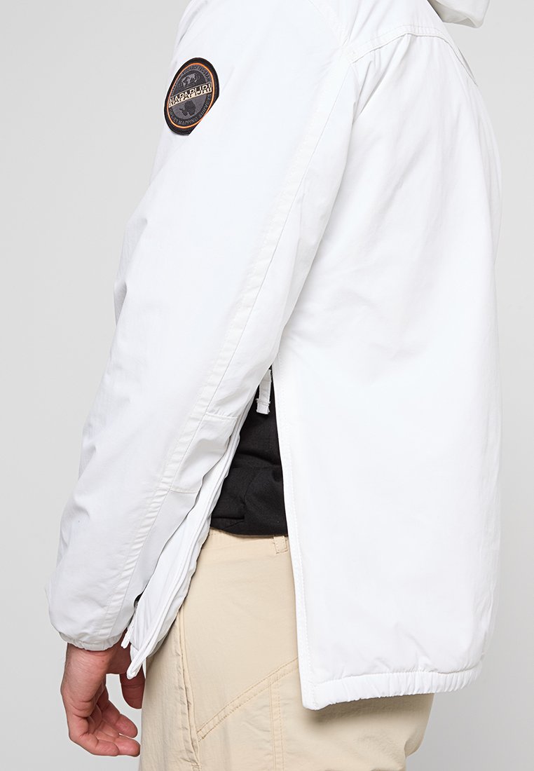 Giacca leggera bianca con apertura laterale con cerniera, caratterizzata da una toppa rotonda nera e arancione sul braccio superiore.