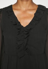 Abito nero con scollatura a V, dettagli arricciati e ricami floreali. Materiale testurizzato con gonna fluida e maniche lunghe in chiffon.