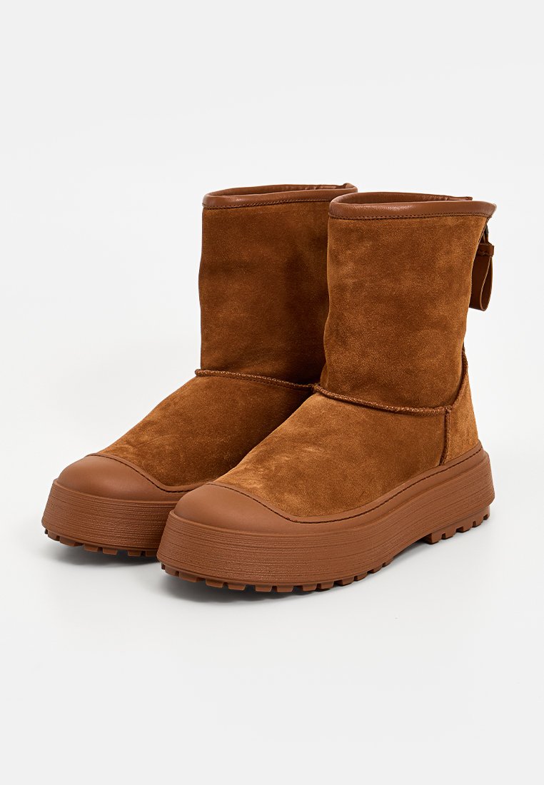 Braune Wildleder-Stiefeletten mit Gummisohle, runder Zehenform und strukturiertem Finish. Verfügt über eine Zuglasche und kontrastierende helle Akzente.
