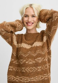 Maglione lavorato a maglia marrone con un motivo geometrico in una tonalità più chiara. La texture morbida, la vestibilità ampia e le maniche larghe aumentano il comfort.