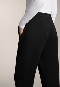 Čierne nohavice s elastickým pásom, so bočnými vreckami a hladkým povrchom. Nosené s priliehavým dlhým rukávom, čiastočne viditeľným.