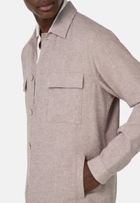 Chaqueta de camisa de lino rosa claro con cuello puntiagudo, botones frontales, dos bolsillos en el pecho y un bolsillo lateral para un look casual.