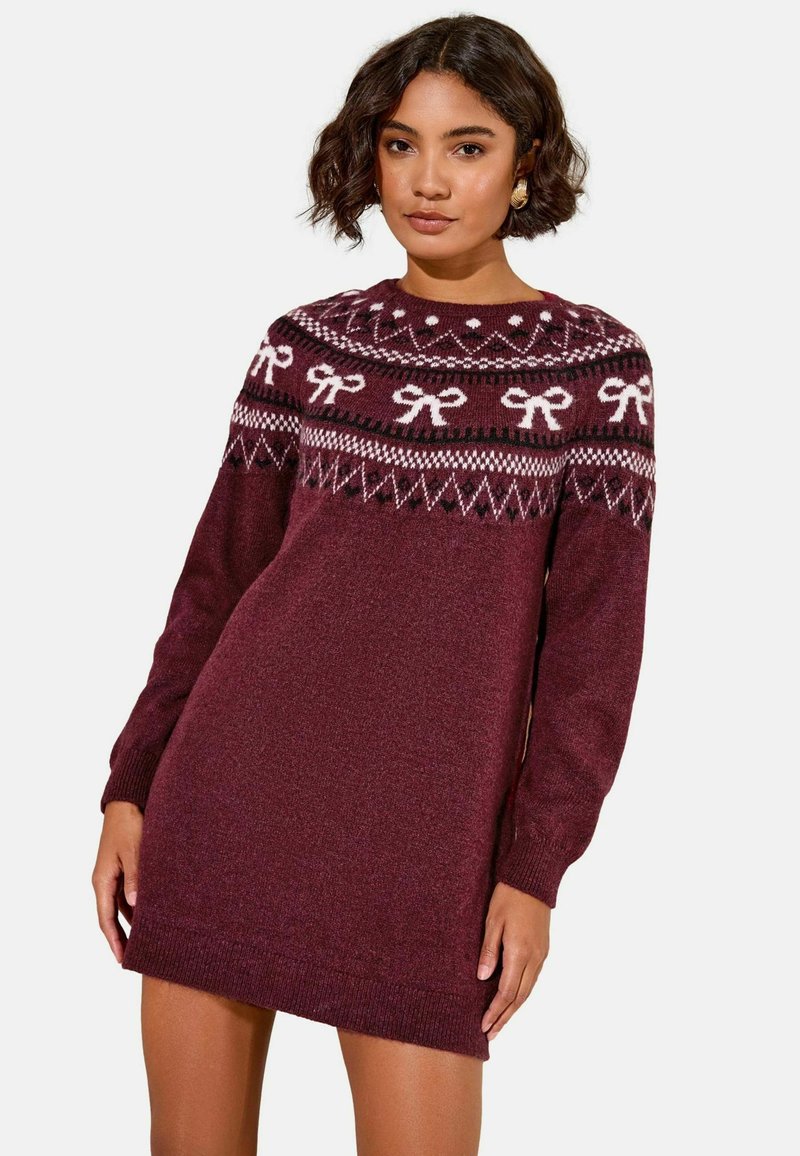Abito maglione bordeaux in un morbido filato, caratterizzato da un motivo Fair Isle con fiocchi bianchi e forme geometriche lungo lo scollo e le maniche.