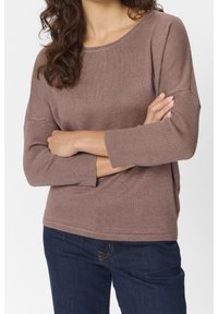 Top marrone a coste con maniche a tre quarti e scollatura ampia, abbinato a jeans in denim scuro. Tessuto liscio e vestibilità comoda.