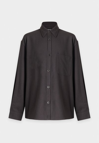 Chemise noire à manches longues avec boutons, col pointu et poche poitrine, présentée sur un fond blanc uni.