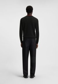 Schwarzer Pullover mit einem roten Akzent am Kragen, kombiniert mit dunklen Hosen. Das Outfit zeichnet sich durch ein schlichtes, tailliertes Design und eine glatte Textur aus.