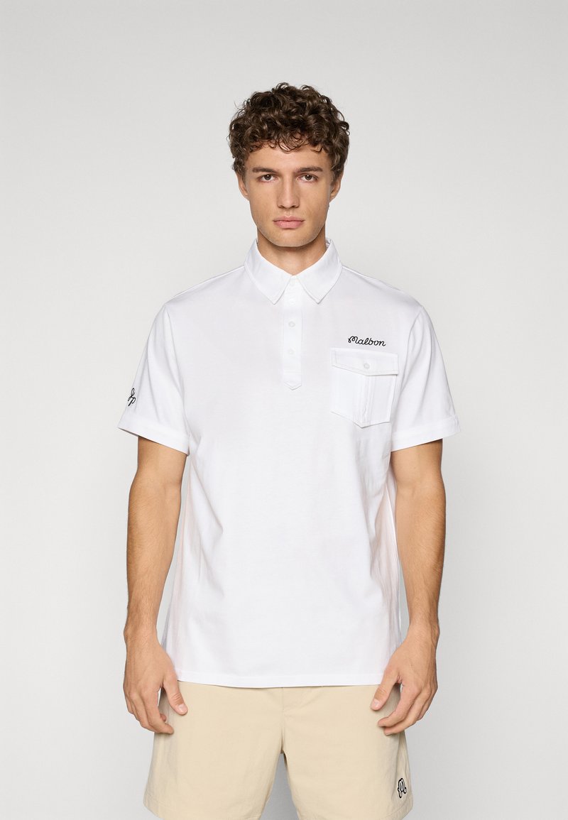 Hvit polo-shirt laget av bomull, med knapp-ned krage, korte ermer, en frontlomme, og broderte tekst på brystet.
