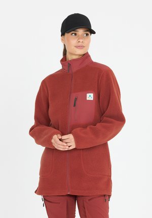Veste en polaire rouge avec une poche zippée, un col haut et une texture douce ; associée à un pantalon rouge. Comprend un patch logo sur la poitrine.