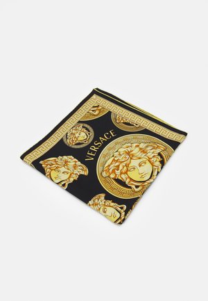 Écharpe Versace noire et dorée avec motifs répétés de tête de Méduse et détail de bordure à motif clé grecque, pliée sur fond blanc.