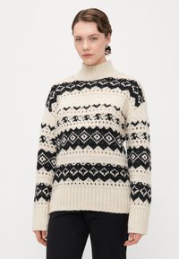 Cremfarbener Strickpullover mit schwarzen geometrischen Mustern, hohem Kragen und geripptem Saum. Verfügt über lange Ärmel und eine lässige Passform.