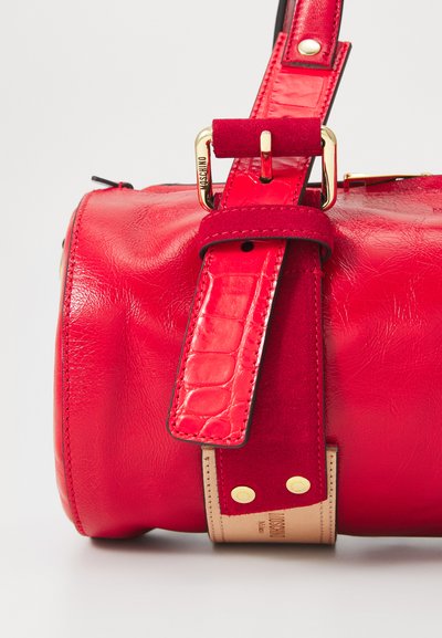 Sac à main en cuir rouge avec une finition texturée, doté d'une bandoulière en suède, de accents en or et d'un logo signature près de la base.
