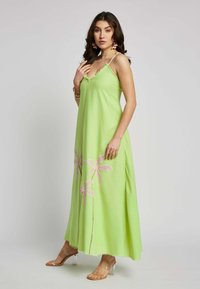 Grünes Maxikleid mit fließender Silhouette. Es hat Spaghettiträger, rosa Blumenstickerei am Saum und einen leicht ausgefransten Rand.
