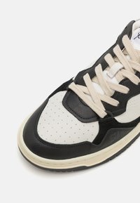Baskets avec un capuchon de orteil en cuir noir, tige en cuir blanc avec des perforations, lacets crème et semelle en caoutchouc texturée.