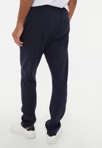 Sudadera azul marino con una textura suave, cinturilla elástica y un bolsillo trasero, combinada con zapatillas blancas con un acento negro en el talón.