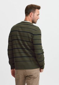 Groene gebreide trui met marineblauwe strepen, ronde hals, geribde manchetten en onderrand, gestructureerde stof, gedragen over beige broeken.