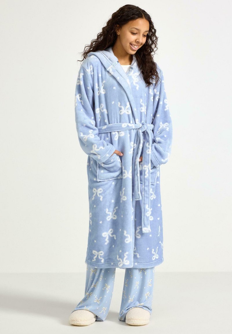 Jasnoniebieski miękki szlafrok z białymi wzorami kokard, dwie przednie kieszenie, pasek i kaptur, w komplecie z pasującymi spodniami. Miękka struktura.