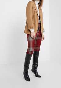 Beżowa marynarka w luźnym fasonie, biała golfowa bluzka, czerwone spodnie w kratę i czarne kozaki do kolan na obcasie z ostrym noskiem.