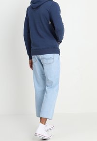 Sudadera con capucha de color marino con bolsillo tipo canguro, combinada con pantalones vaqueros cortos de color azul claro y zapatillas blancas. Corte holgado y diseño casual.