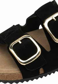 Sandale en suède noire avec deux boucles dorées, un milieu de semelle en liège texturé et une semelle en caoutchouc à motif zigzag. Découpes le long du design supérieur.