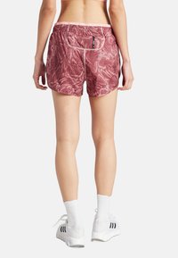 Roze, patroon sportshorts met een trekkoord in de taille, voorzien van een achterzak en contrasterende stiksels, gecombineerd met witte sokken en schoenen.