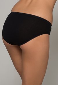 Culotte en coton noir avec une texture lisse, présentant une taille délicate et des bords festonnés, mettant en valeur une coupe hipster classique.