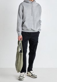 Gray hooded sweatshirt with front pocket, black cargo pants, green tote bag, and cream sneakers with black and green accents.
