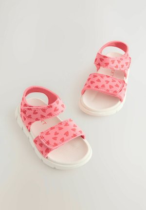 Sandales pour enfants roses avec des motifs de cœurs, sangles Velcro réglables et une semelle texturée blanche pour une meilleure adhérence. Conçues pour le confort et le style.