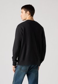 Crna majica s dugim rukavima, okruglim izrezom i rebrastim manšetama. Uparena s trapericama svijetloplave boje koje imaju opušteni kroj.