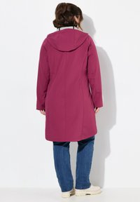 Magenta long jacket with a hood, solid design, smooth texture, side pockets, and a straight cut, paired with blue jeans and light footwear.