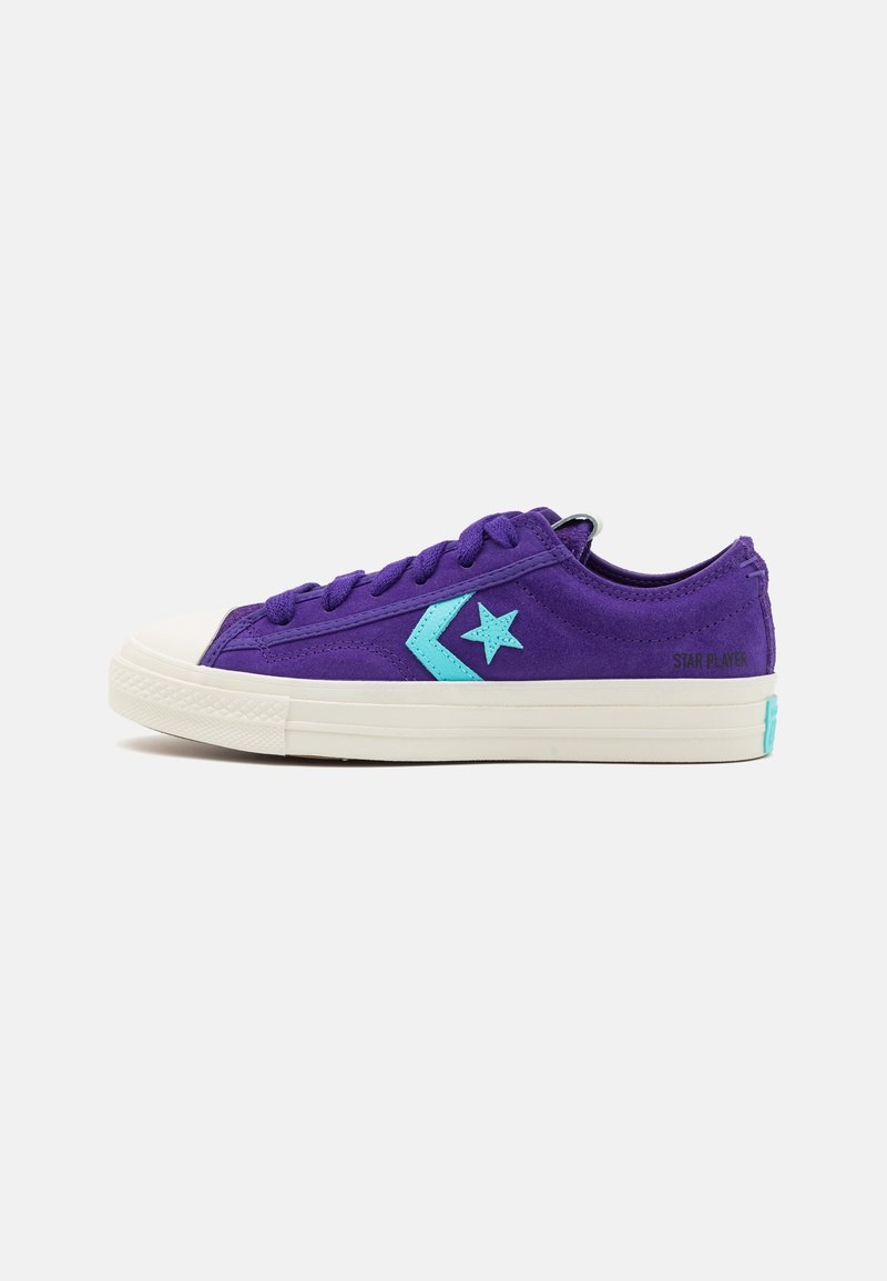Baskets basses violettes avec étoile turquoise et logo chevron, semelle en caoutchouc blanche et lacets, vues de côté.