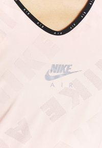 Nike sports top in light pink with a textured finish, featuring a black crew neckline and a silver logo print along with patterned accents.