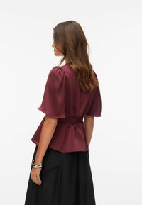 Mørkerød bluse med korte puffermede ermer, innsnevret midje og en flytende kant. Brukt sammen med et svart skjørt, glatt tekstur.