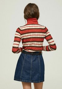 Stickad röd, krämfärgad och brun randig polotröja med strukturerat mönster, kombinerad med en mörk denim mini kjol och svart bälte.