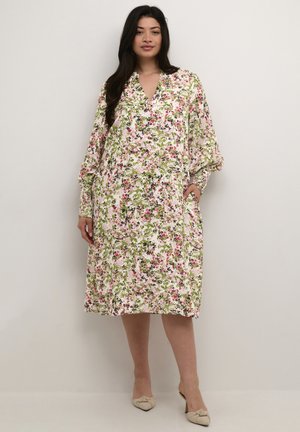 Robe midi florale blanche avec des motifs roses et verts, dotée d'un décolleté en V, de longues manches et de poches, fabriquée en tissu léger.