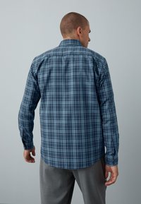 Herrenhemd in Blau mit kariertem Muster, Kragen, langen Ärmeln und geknöpften Manschetten. Der Stoff wirkt glatt, mit einer strukturierten Passform und abgerundetem Saum.