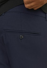 Marineblaue Hose mit einer kleinen Gesäßtasche, die mit einem schwarzen Knopf verziert ist, und einer subtilen Textur im Stoff für ein zusätzliches Design.