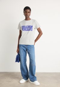 Gray cotton t-shirt with bold purple text. Paired with blue wide-leg jeans and white sneakers. Holding a small blue handbag.