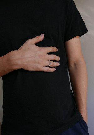 Silver ring worn on a left hand, resting on a black cotton shirt. Skin is lightly textured, with prominent veins visible on the hand.